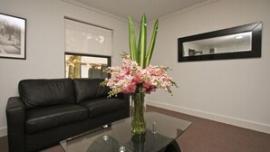 A modern living room with a glass coffee table, a black leather sofa, and a vase of pink flowers. - One Bedroom Apartment (Newcastle West)