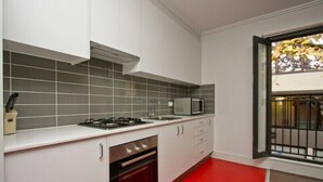 A kitchen with white cabinets, a red floor, a gas stove, a microwave, and a window with a view of trees. - One Bedroom Apartment (Newcastle West)