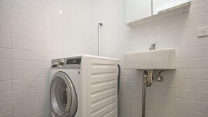 Un espace buanderie compact comprenant un lave-linge à chargement frontal et un évier.
