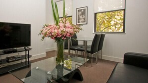 Une chambre moderne avec une table en verre, un téléviseur, un vase de fleurs et une fenêtre donnant sur des arbres.