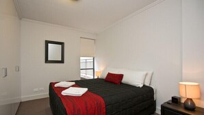 Une chambre d’hôtel avec un lit, une table de chevet, une lampe et une fenêtre avec des stores.