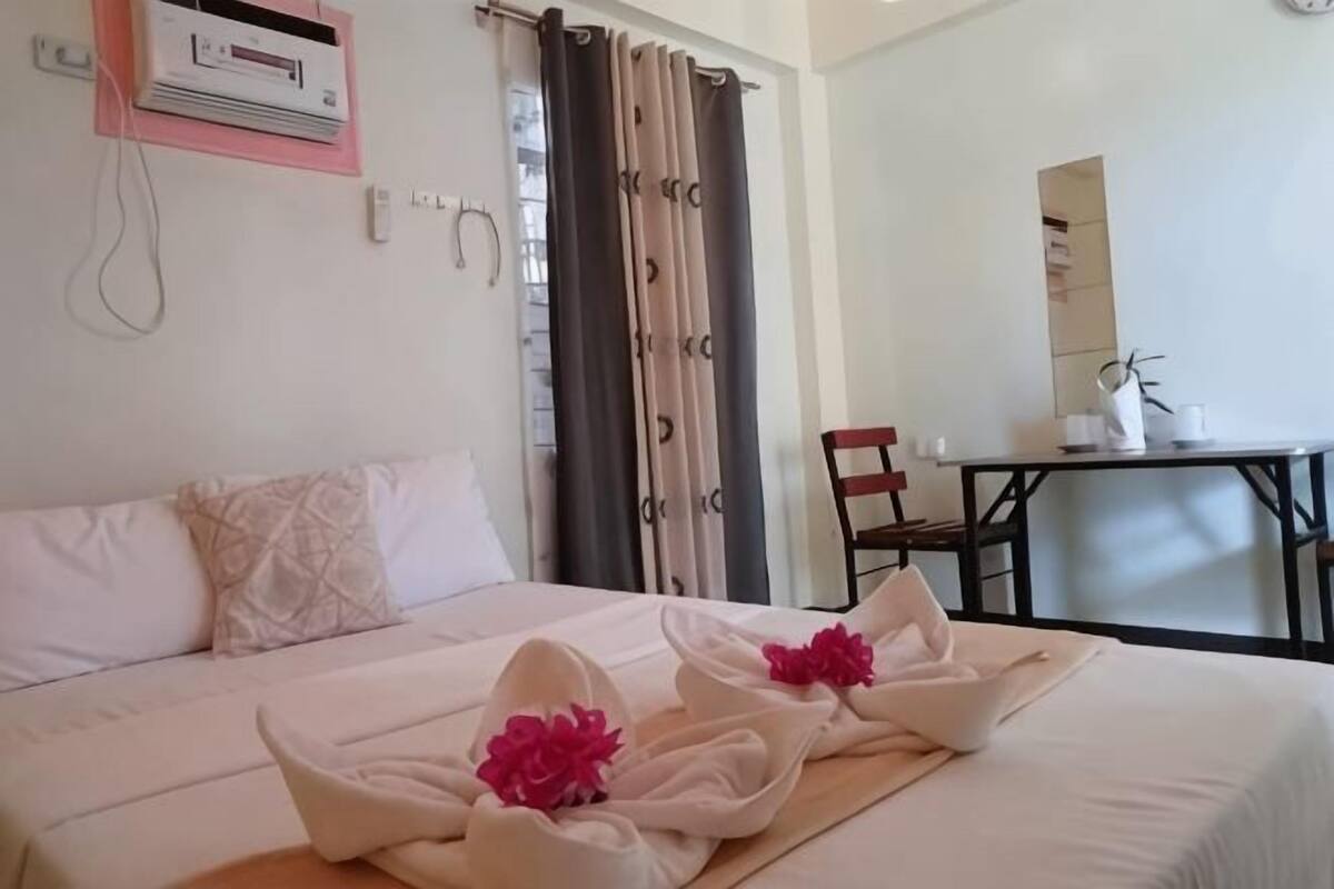 A hotel room with a bed, a desk, a chair, and a mirror.