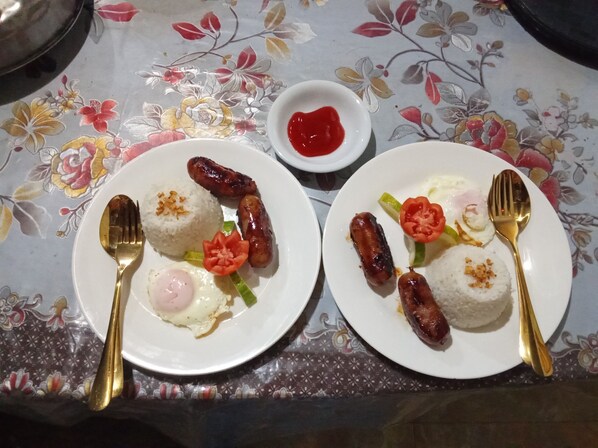 Two plates of food with sausages, rice, and eggs on a table with a floral tablecloth.