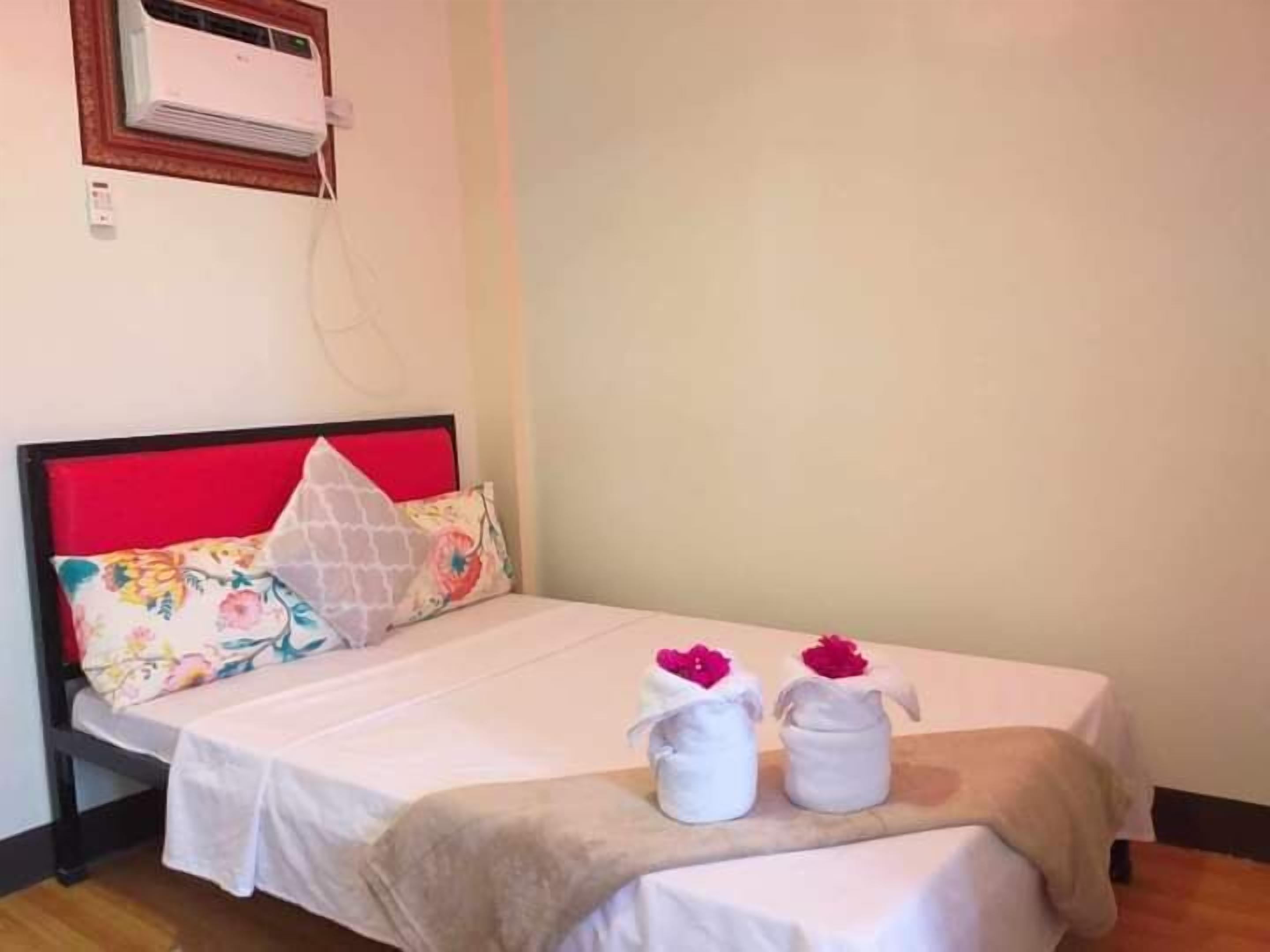 A single bed with a red headboard, white bedding, and two white towels with pink flowers on the bed.