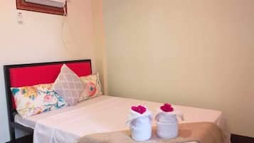 A single bed with a red headboard, white bedding, and two white towels with pink flowers on the bed.
