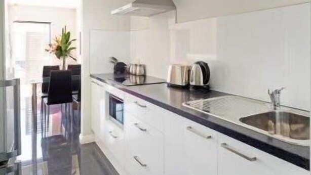 A modern kitchen with white cabinets, a black countertop, and stainless steel appliances. - One Bedroom Disability Access (Cardiff)
