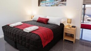 Ein modernes Hotelzimmer mit einem großen Bett, einem Nachttisch mit Lampe und Blick ins Freie durch eine Glastür.