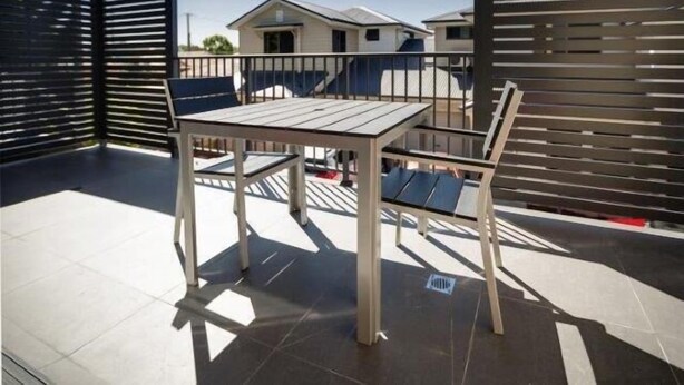 Eine Terrasse mit Tisch und Stühlen, ein Metallzaun und ein Blick auf ein Wohngebäude im Hintergrund.