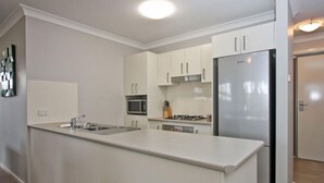 A modern kitchen with white cabinets, a stainless steel refrigerator, a microwave, and a gas stove. - Cardiff Two Bedroom Villa (Cardiff)