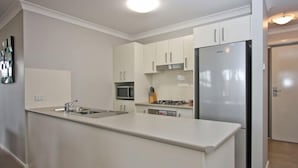 A modern kitchen with white cabinets, a stainless steel refrigerator, a microwave, and a gas stove. - Cardiff Two Bedroom Villa (Cardiff)