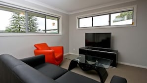 A modern living room with a black sofa, a red chair, a glass coffee table, and a flat-screen TV on a black stand. - Cardiff Two Bedroom Villa (Cardiff)