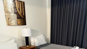Ett hotellrum med två sängar, ett nattduksbord med en lampa, en tavla på väggen och en mörk gardin.