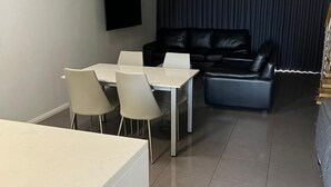 Ett modernt vardagsrum med en matplats, en svart lädersoffa och en platt-TV som är monterad på väggen.