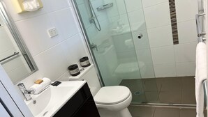 Ett modernt badrum med en duschavdelning med glasväggar, en vit toalett, en svart tvättställsmöbel med en handduk och tvål, och en vit handduk som hänger på väggen.