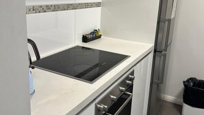 Ett modernt kök med vita skåp, en svart induktionshäll, en ugn i rostfritt stål och ett kylskåp.