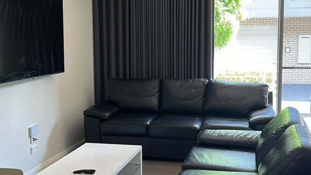 A modern living room with a black leather sofa, a white coffee table, and a flat-screen TV mounted on the wall. - Two Bedroom Apartment (Charlestown)