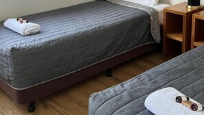 A small, neatly arranged bedroom with a single bed, a bedside table with a lamp, and a window with blinds. - Two Bedroom Apartment (Charlestown)