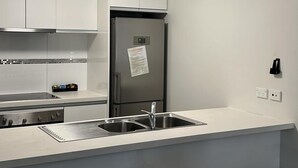A modern kitchen with white cabinets, a stainless steel refrigerator, a built-in oven, and a granite countertop. - Two Bedroom Apartment (Charlestown)