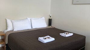 A neatly made bed with a brown quilt, white pillows, and two towels folded on the bed.