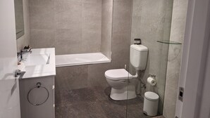 A modern bathroom with a bathtub, toilet, and glass shower enclosure.