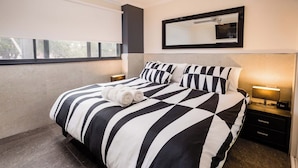 A modern hotel room with a large bed, striped bedding, a bedside lamp, a nightstand, and a window with a view.