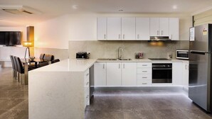 A modern kitchen with white cabinets, a central island, stainless steel appliances, and a dining area with a table and chairs.