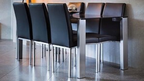 A modern dining area with a round table and six black chairs with metallic legs. A floor lamp with multiple light bulbs is positioned to the left.