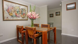 A dining area with a wooden table and chairs, a vase of flowers, and a large abstract painting on the wall. - Two Bedroom Apartment (Newcastle)
