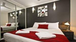 A hotel room with a large bed, a bedside table with a lamp, a mirror, and a wall with abstract art. - Two Bedroom Apartment (Newcastle)