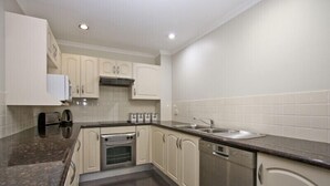 A compact kitchen with white cabinets, a stainless steel sink, and a built-in oven. - Two Bedroom Apartment (Newcastle)