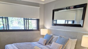 A neatly made bed with a striped blanket, two bedside lamps, and a large mirror above it. - Two Bedroom Apartment (Newcastle)