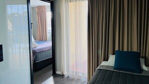 A hotel room with a bed, a window with curtains, and a view of the outside. - Two Bedroom Interconnect (Hamilton)