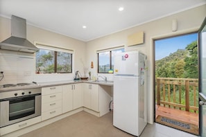 A modern kitchen with white cabinets, a stove, and a refrigerator. - Hosts on the Coast Views from the Top (Cooks Beach)