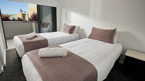 A hotel room with two beds, a balcony, and a view of buildings. - Two Bedroom Apartment (Carrington)