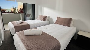 A hotel room with two beds, a balcony, and a view of buildings. - Two Bedroom Apartment (Carrington)