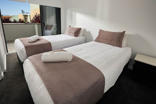 A hotel room with two beds, a balcony, and a view of buildings.