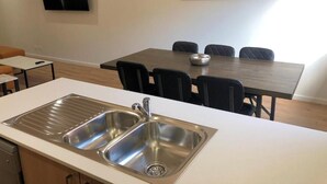 A modern kitchen with a double sink, a dining area with a table and chairs, and a large abstract painting on the wall. - Two Bedroom Apartment (Waratah West)