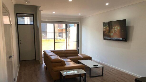 A modern living room with a sofa, coffee table, and a TV mounted on the wall. - Two Bedroom Apartment (Waratah West)