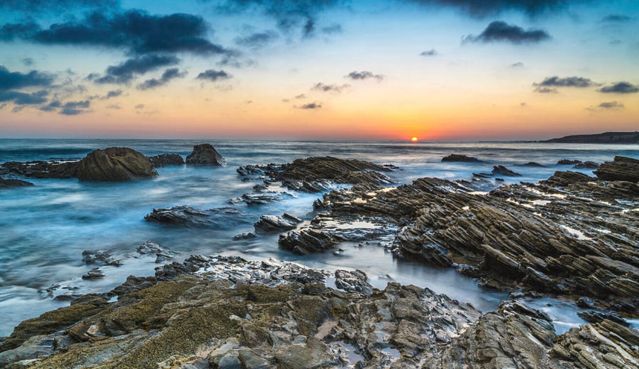 A rocky shoreline with a sunset in the background.