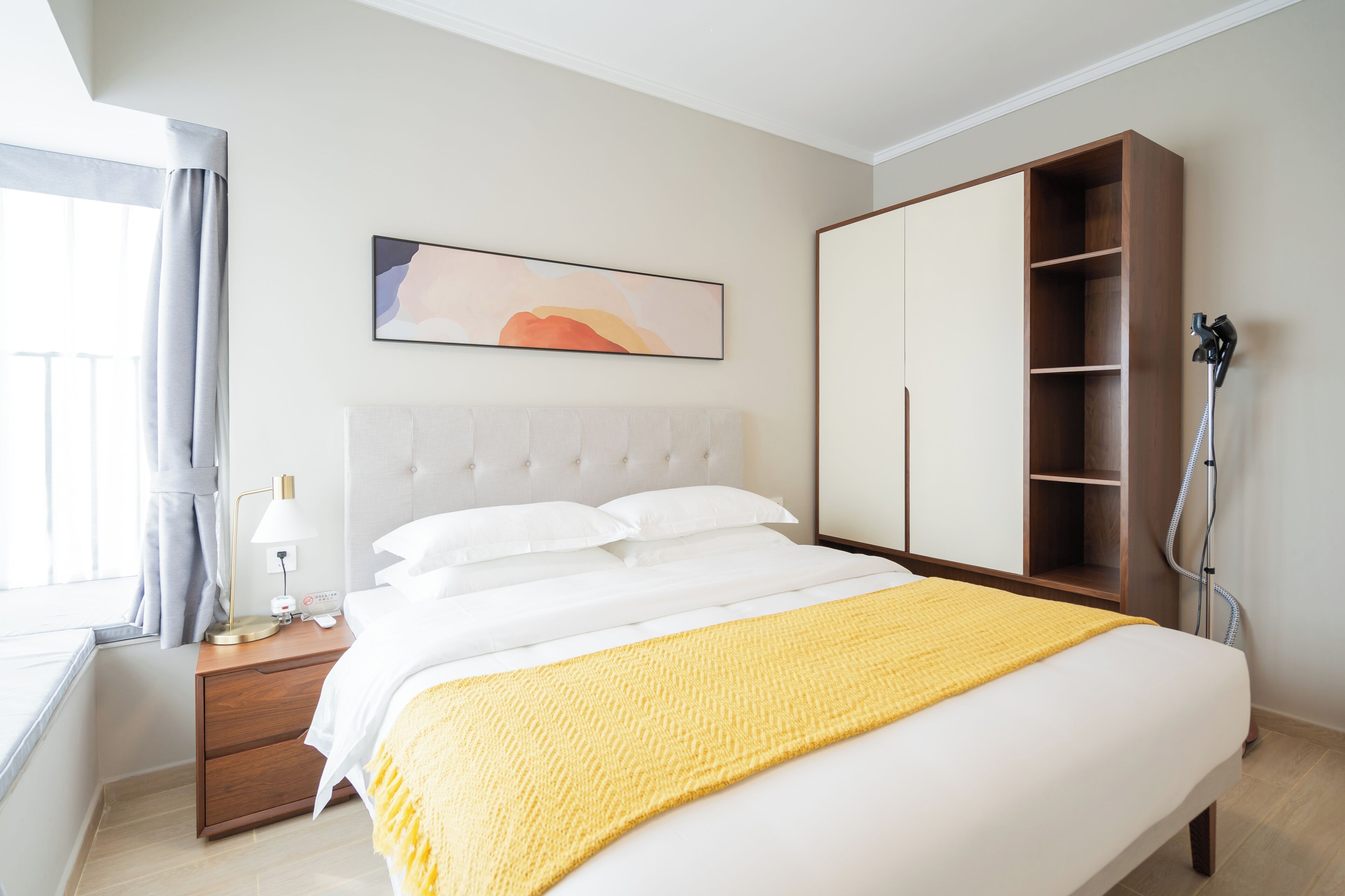Hotelkamer met een groot bed, een houten garderobe, een nachtkastje met lamp en een raam met gordijnen.