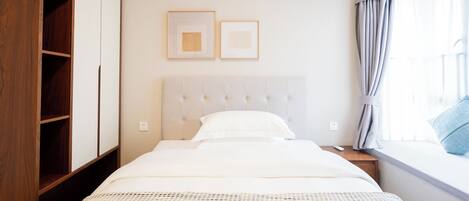 A neatly arranged hotel room with a bed, a wardrobe, and a window with curtains.