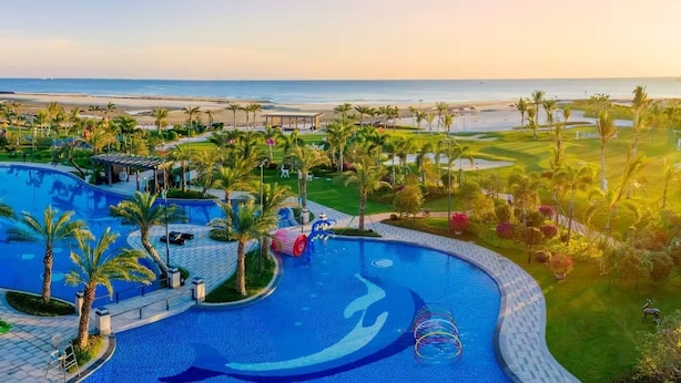 A resort with a large swimming pool, palm trees, and a view of the beach. - home at beach (Beihai)