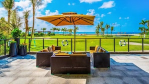 A patio with wicker furniture and a large umbrella, overlooking a golf course with palm trees and a clear blue sky. - home at beach (Beihai)
