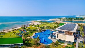 A resort with a large swimming pool, a beach, and a modern building with a solar panel. - home at beach (Beihai)