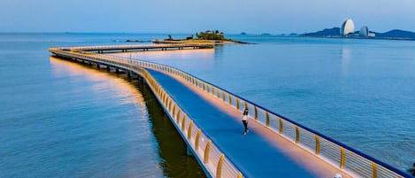 Un largo puente peatonal sobre el agua, con una persona caminando y otra tomando una fotografía.