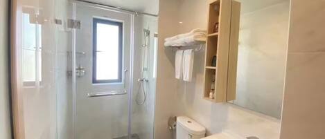 Un baño moderno con ducha de vidrio, inodoro blanco y lavamanos con espejo arriba.