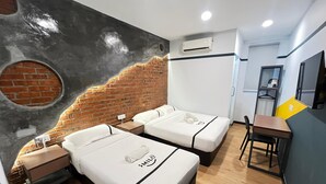 Habitación de hotel con dos camas, un escritorio, una silla, una mesita, unidad de aire acondicionado y un mural de ladrillo.