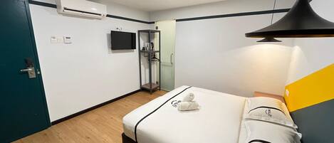 A modern hotel room with a bed, a wardrobe, an air conditioning unit, a television, and a door.
