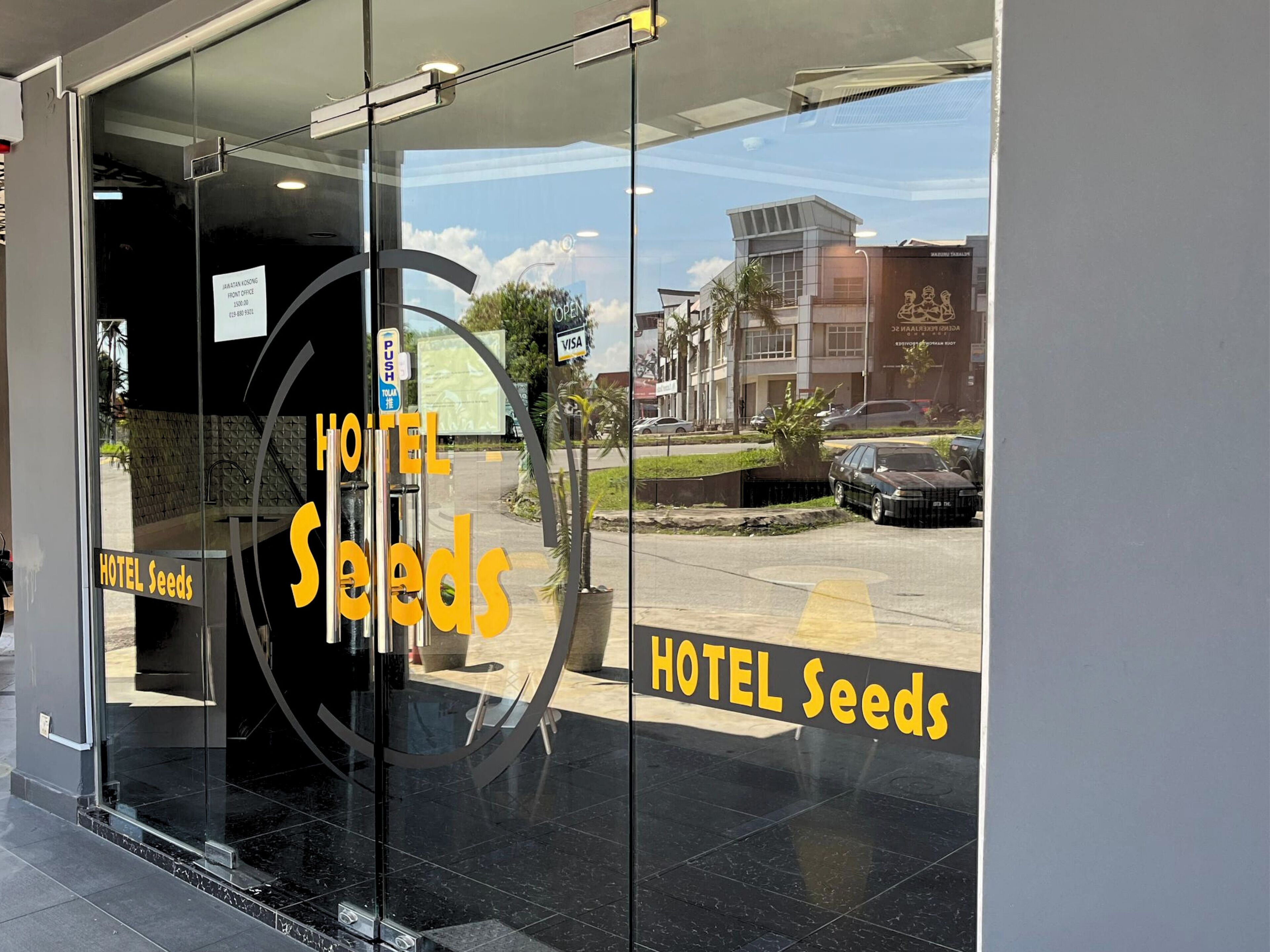 A hotel entrance with a glass door, a sign reading "HOTEL Seeds", and a view of the street outside.