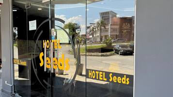 A hotel entrance with a glass door, a sign reading "HOTEL Seeds", and a view of the street outside.